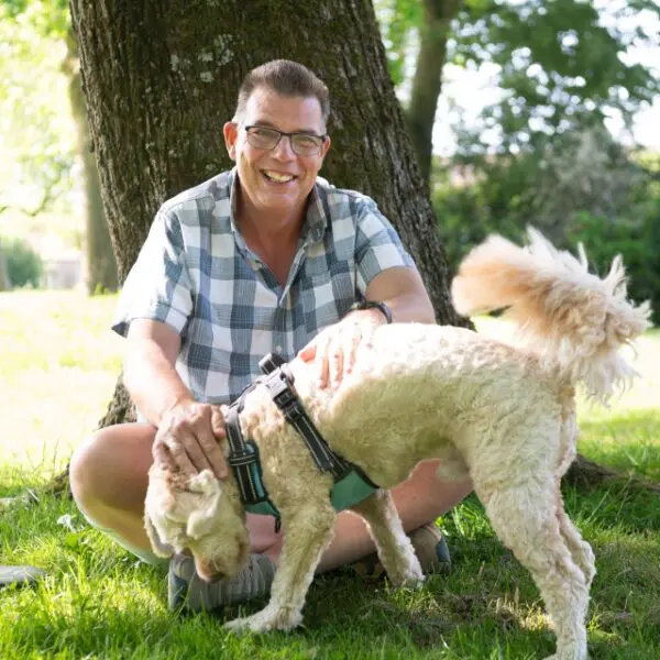 Portret van een persoon met een hond in een groene buitenomgeving.