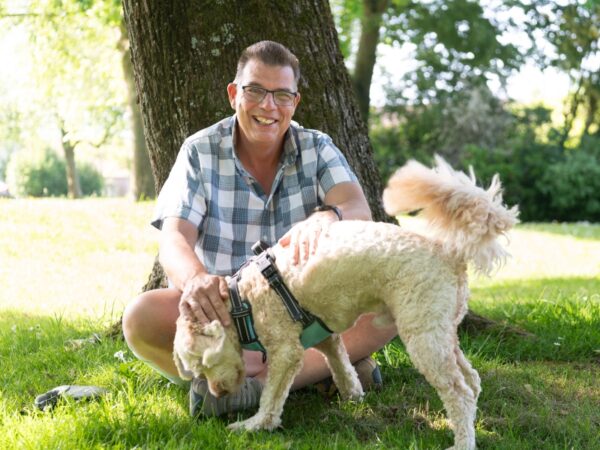 Portret van een persoon met een hond in een groene buitenomgeving.